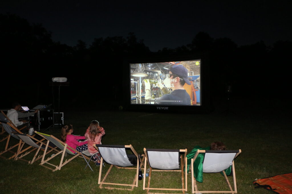 Ludzie siedzą na leżakach na zewnątrz i oglądają film wyświetlany na ekranie